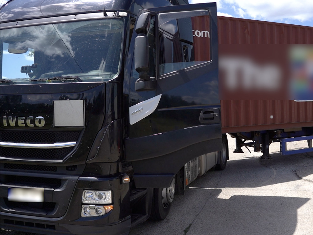 Czarny samochód ciężarowy marki Iveco stojący obok kontenera na placu załadunkowym.