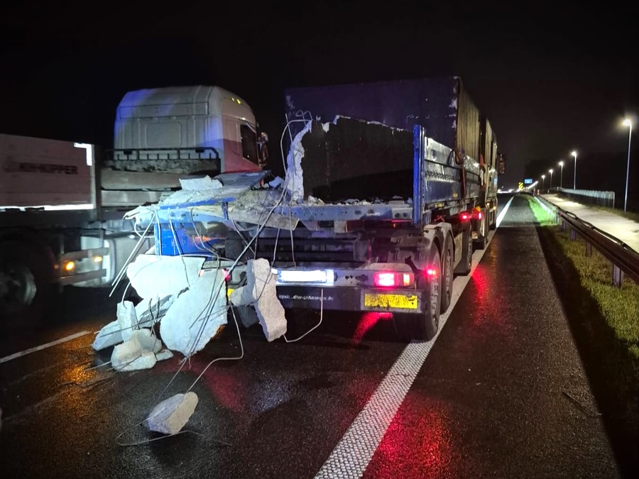 Ciężarówka z uszkodzonym ładunkiem betonowym stoi na drodze nocą, obok innych pojazdów.