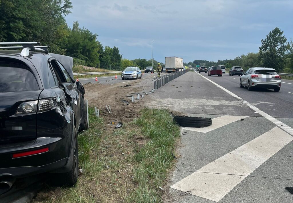 Czarny SUV z uszkodzoną karoserią stoi na poboczu drogi, obok ruchliwej autostrady z pojazdami w tle.