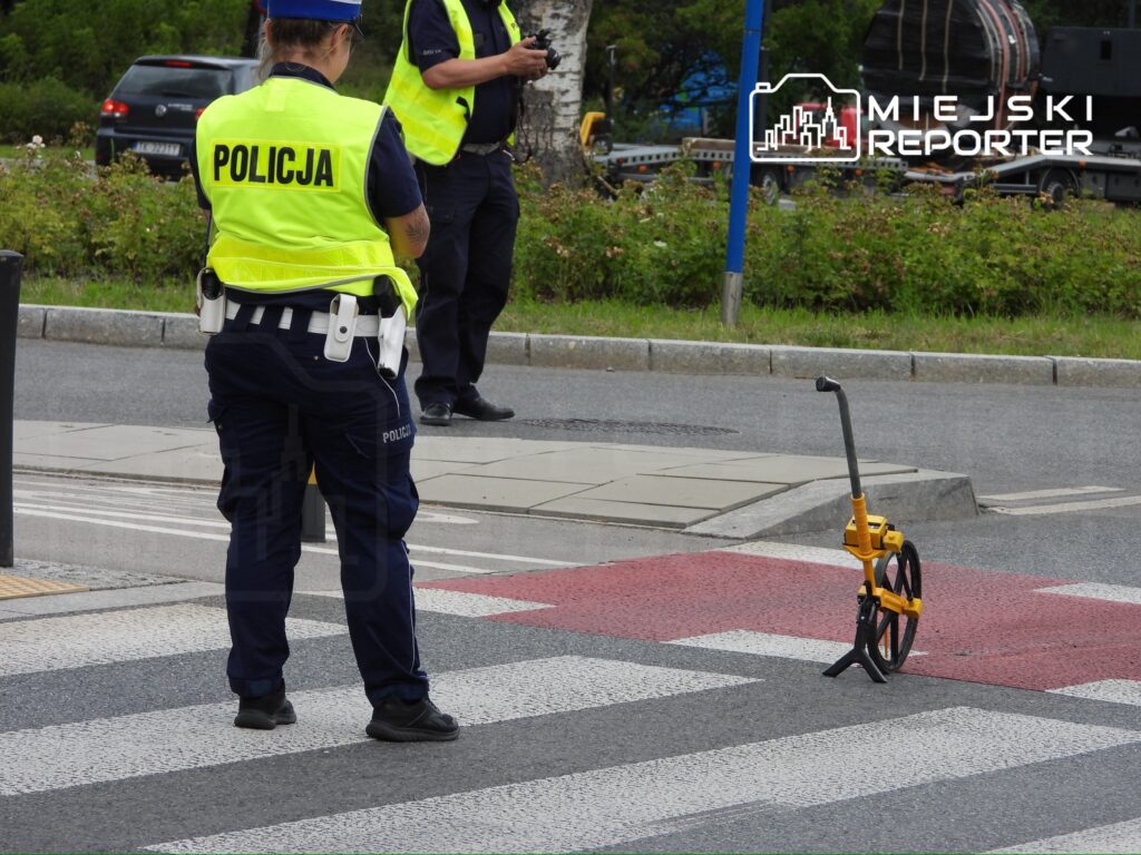 Policjantka w kamizelce odblaskowej mierzy odległość na przejściu dla pieszych za pomocą dalmierza.
