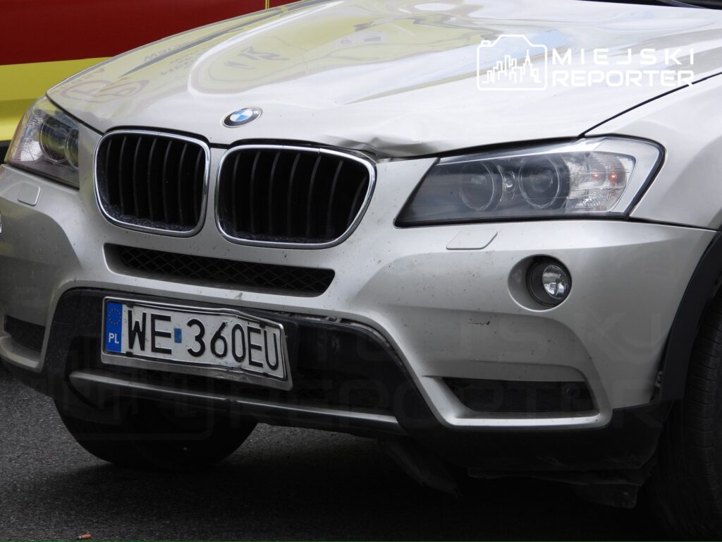 Uszkodzony samochód osobowy marki BMW zaparkowany na ulicy, z widocznym wgnieceniem na masce.
