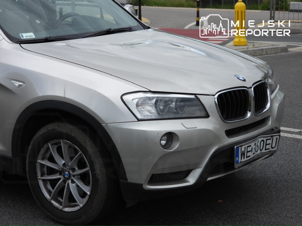 Srebrny samochód marki BMW zaparkowany na drodze, z widocznymi zarysowaniami na karoserii i brudnymi felgami.