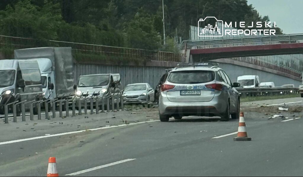 Zdarzenie drogowe z udziałem kilku pojazdów na ruchliwej drodze, w tle widoczne samochody i bariera ochronna.