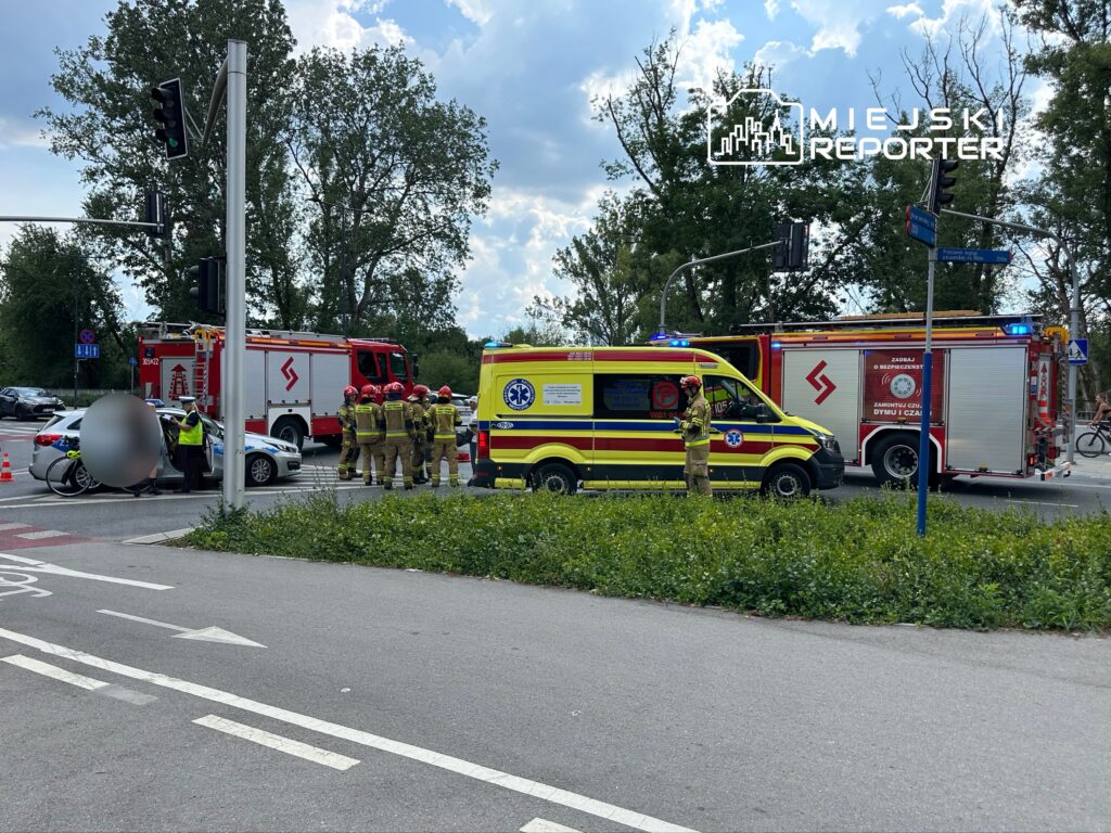 Grupa strażaków i ratowników medycznych pracuje przy wypadku drogowym, obok zaparkowanych pojazdów.