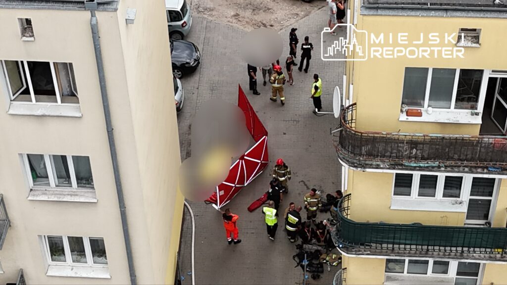 Grupa ratowników i strażaków pracuje na podwórku, obok rozłożonej czerwonej konstrukcji.