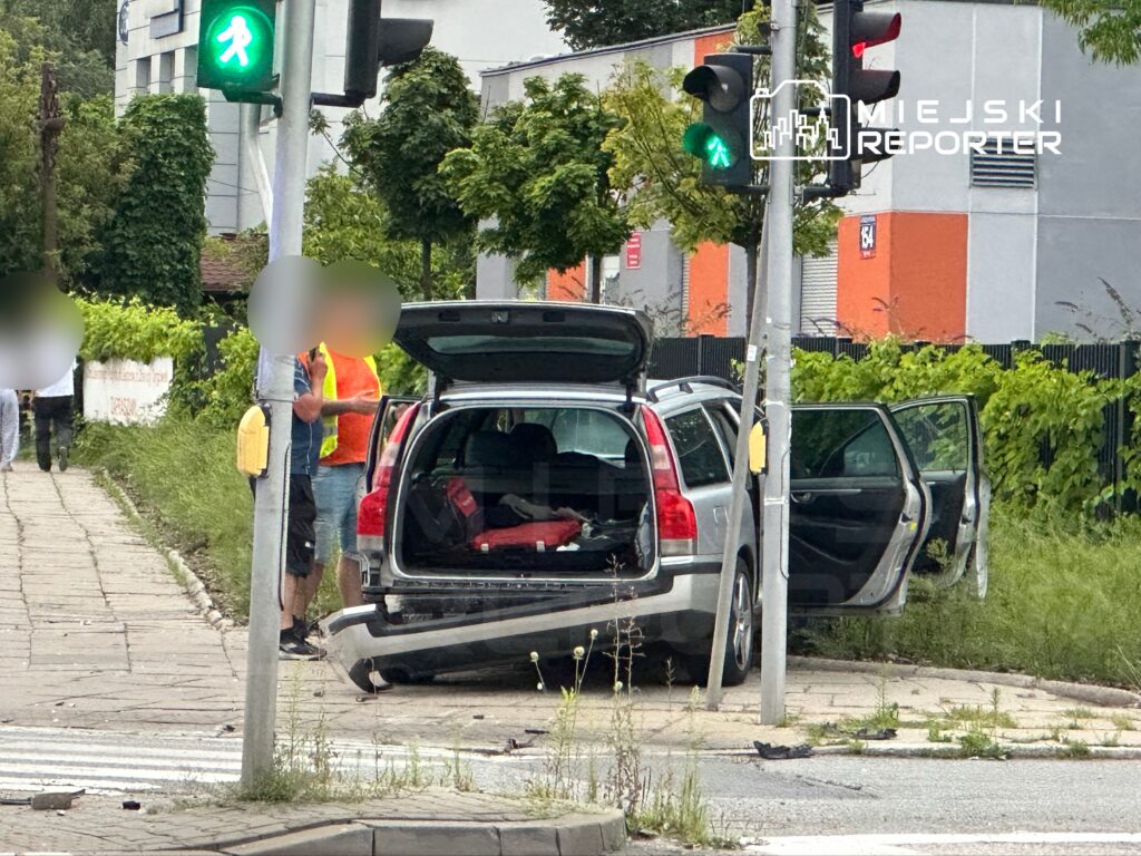 Mężczyzna w kamizelce odblaskowej rozmawia z innym mężczyzną obok otwartego bagażnika samochodu na chodniku.