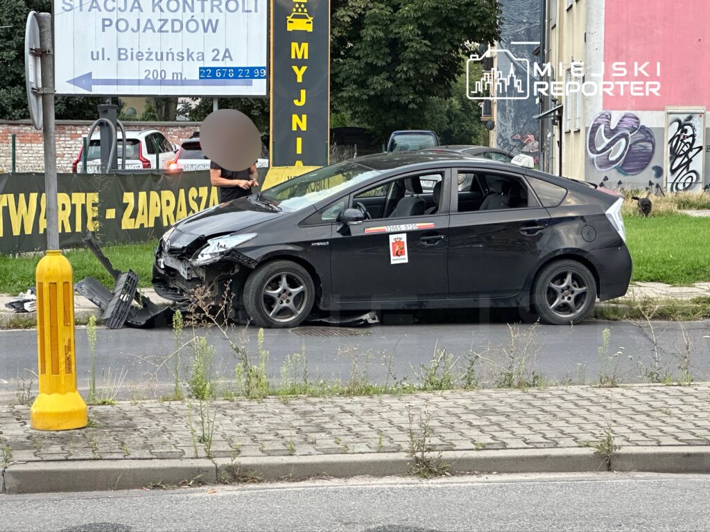 Czarny samochód osobowy z uszkodzoną przednią częścią stoi na poboczu, a obok mężczyzna sprawdza jego stan.