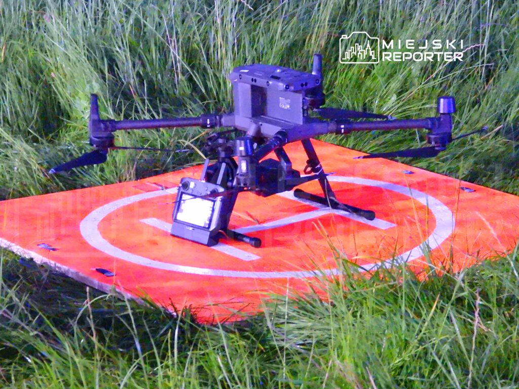 Dron lądował na pomarańczowej platformie w trawie, gotowy do dalszego działania.
