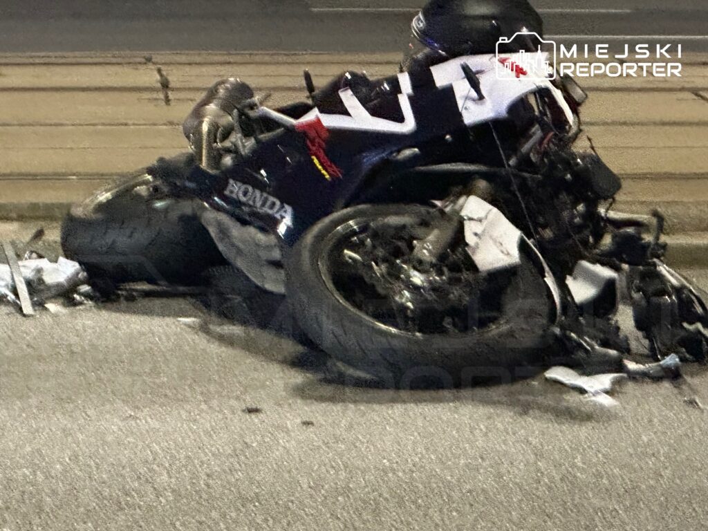 Zniszczony motocykl leżący na drodze, otoczony fragmentami odzieży i pozostałościami po wypadku.