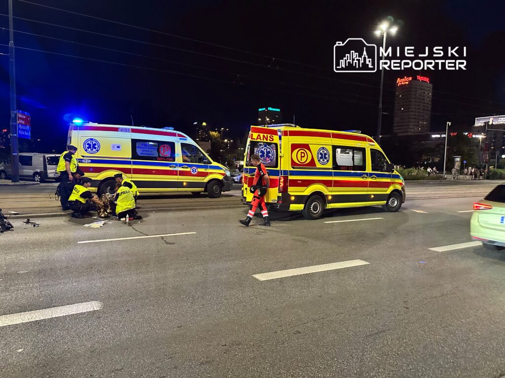 Zespół ratowników medycznych udziela pomocy poszkodowanemu na jezdni, obok dwóch ambulansów.