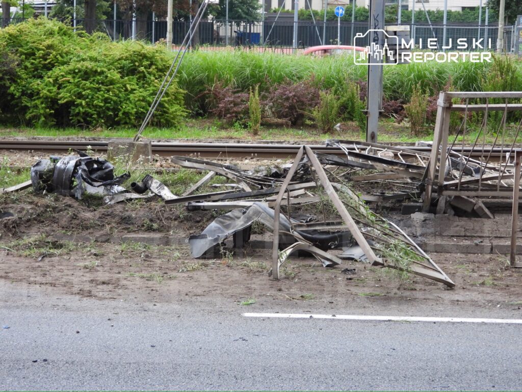 Zniszczona infrastruktura tramwajowa z metalowymi elementami i resztkami pojazdu leżącymi na ziemi.