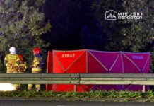 Grupa strażaków w mundurach rozmawia obok czerwonego namiotu z napisem "STRAŻ" przy drodze.