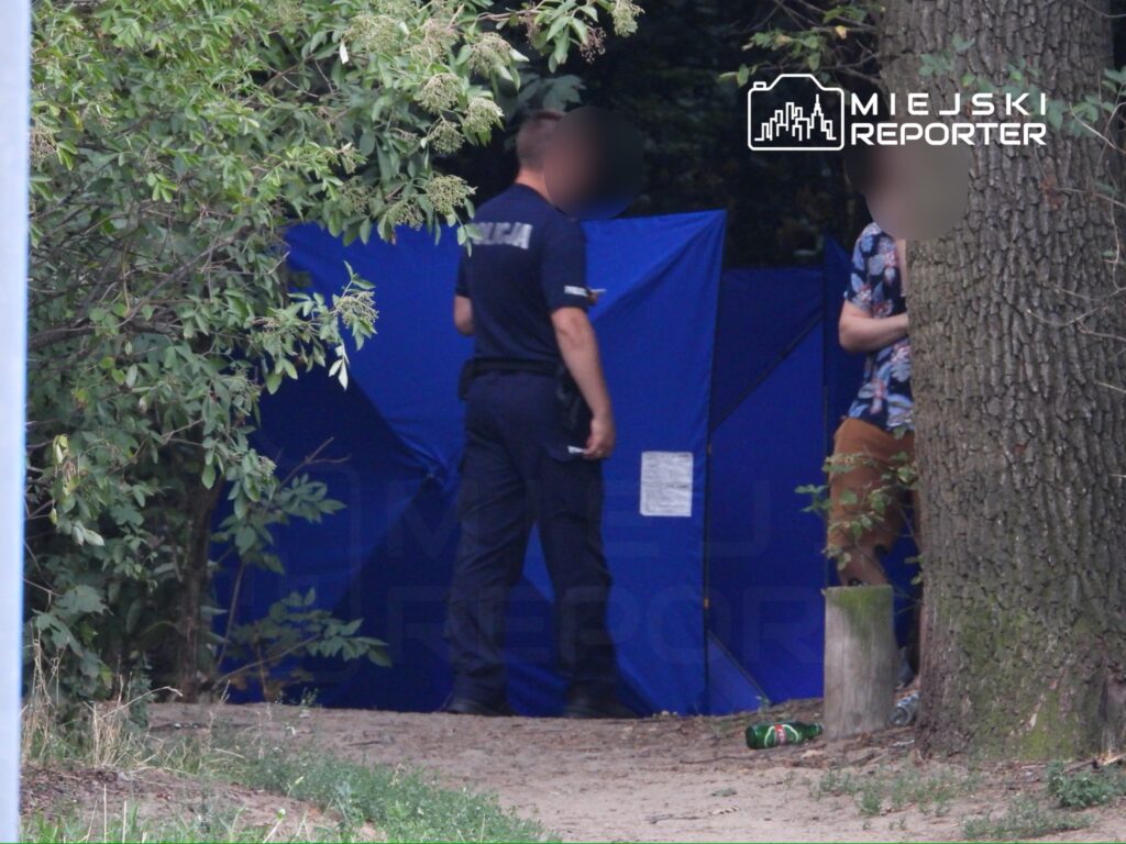 Policjant rozmawia z mężczyzną przy niebieskim namiocie w leśnej okolicy. W tle widoczne śmieci.