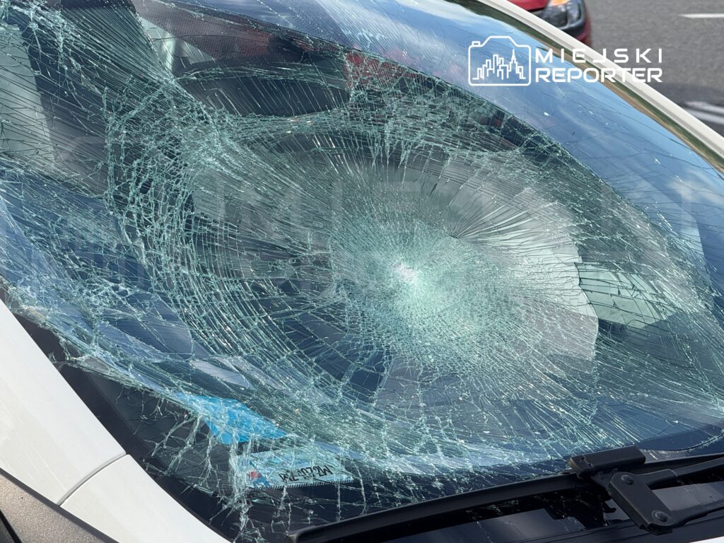 Pęknięta szyba samochodu z widocznymi odłamkami szkła na przedniej szybie, zaparkowanego na parkingu.