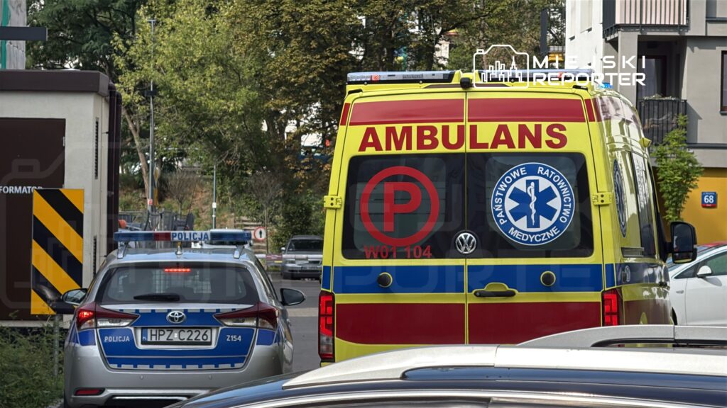 Karetkę pogotowia z napisem "AMBULANS" zatrzymaną przy ulicy, obok policyjnego samochodu.