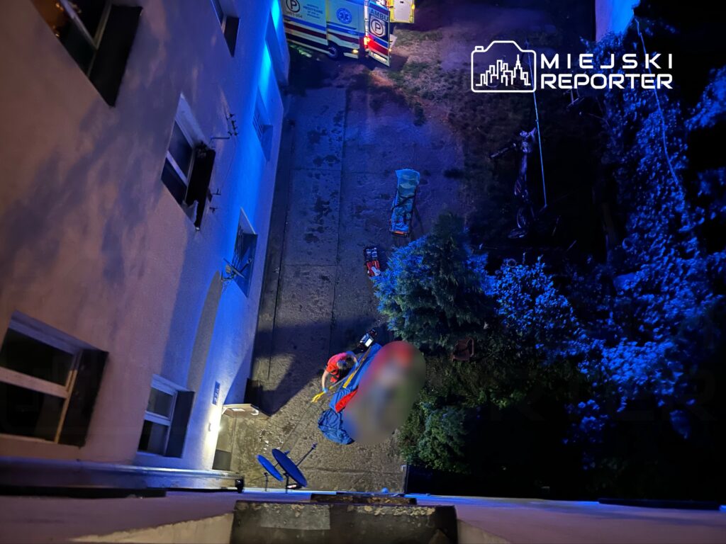 Ratownicy medyczni udzielają pomocy osobie leżącej na ziemi w oświetlonym niebieskim otoczeniu.