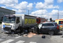 Zderzenie ciężarówki z osobowym samochodem na skrzyżowaniu, wokół obecne służby ratunkowe oraz uszkodzone pojazdy.