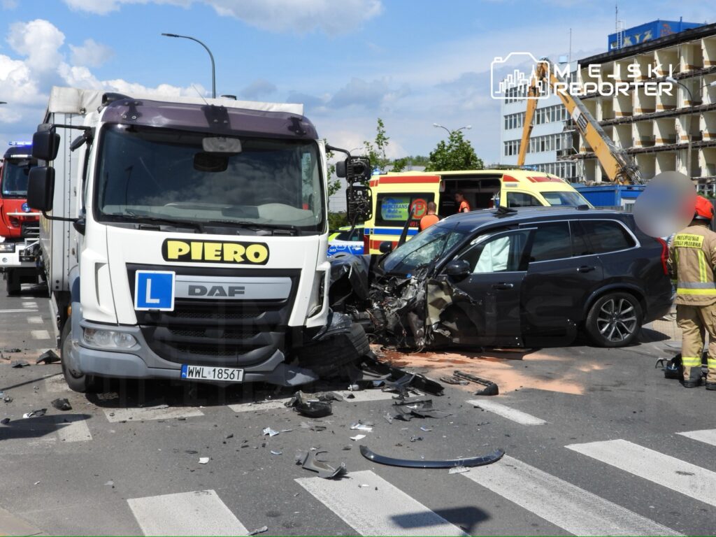 Wielka kolizja drogowa z udziałem ciężarówki i osobowego samochodu na skrzyżowaniu, z rozrzuconymi fragmentami pojazdów.