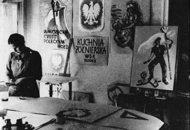 Artysta w pracowni malarskiej przygotowuje prace, otoczony plakatami z motywami patriotycznymi i wojskowymi.