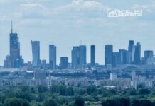Panoramiczny widok na skyline miasta z nowoczesnymi drapaczami chmur, w tle chmury na błękitnym niebie.