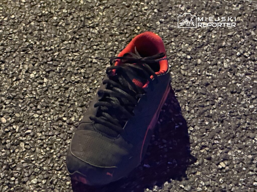 Czarna sportowa sneaker z czerwonymi akcentami leży na asfaltowej nawierzchni.