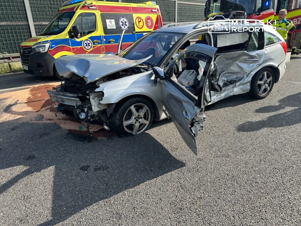 Wypadek drogowy z udziałem samochodu osobowego. Pojazd ma poważne uszkodzenia z przodu i po stronie pasażera. Na miejscu zdarzenia obecne są służby ratunkowe oraz karetka. Widać plamy płynów eksploatacyjnych na jezdni. Akcja ratunkowa trwa.