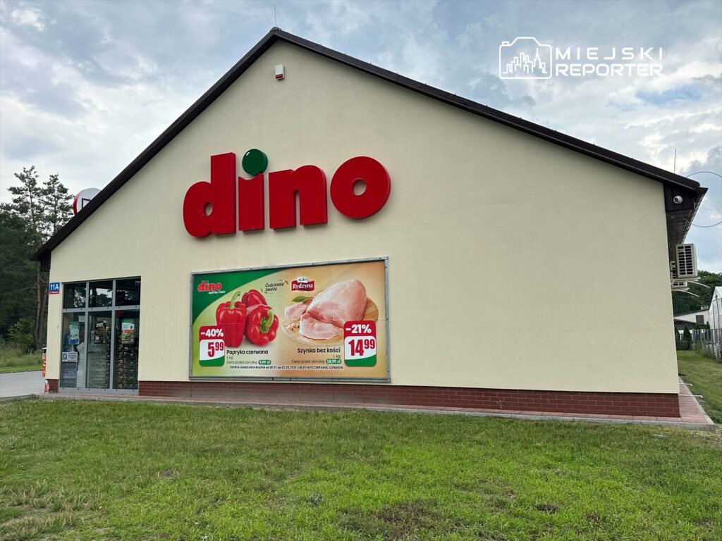 Sklep spożywczy z dużym napisem "dino" na elewacji, z promocjami na paprykę i szynkę na plakacie.