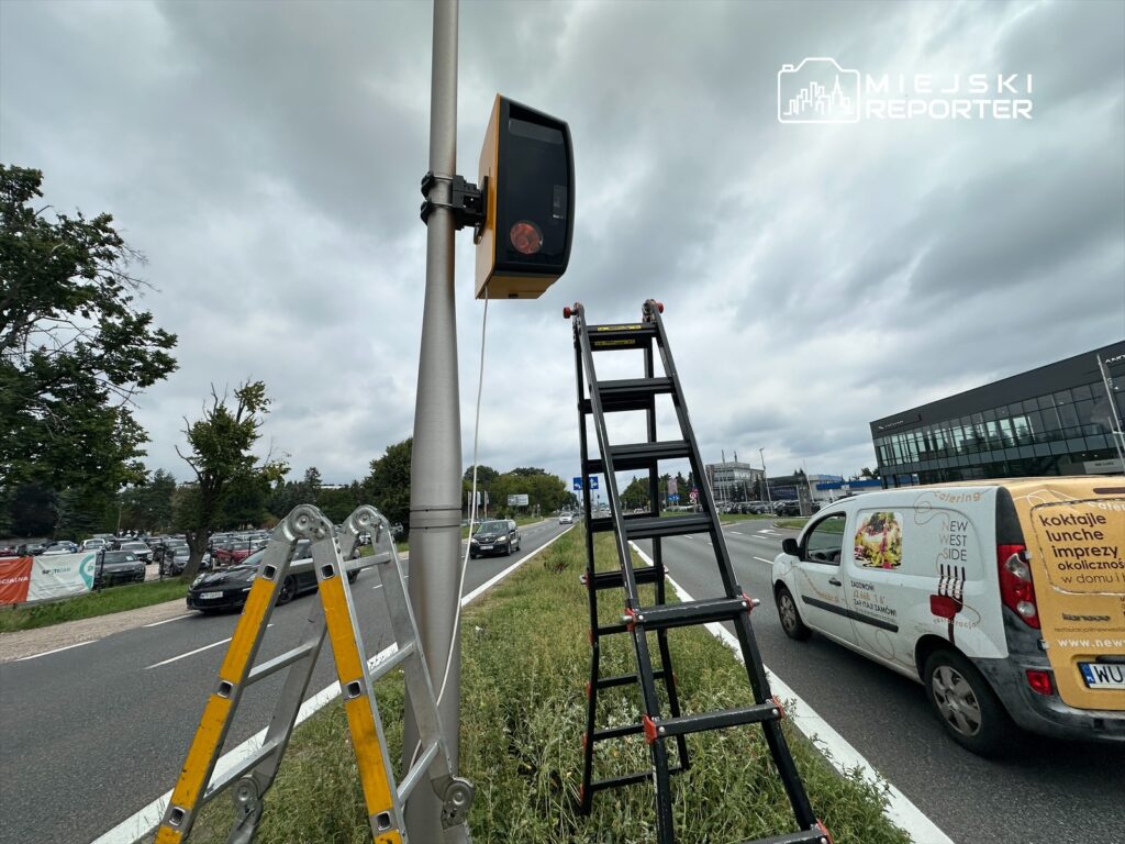 Pracownik wchodzi na drabinę obok nowoczesnego sygnalizatora świetlnego na ruchliwej drodze.