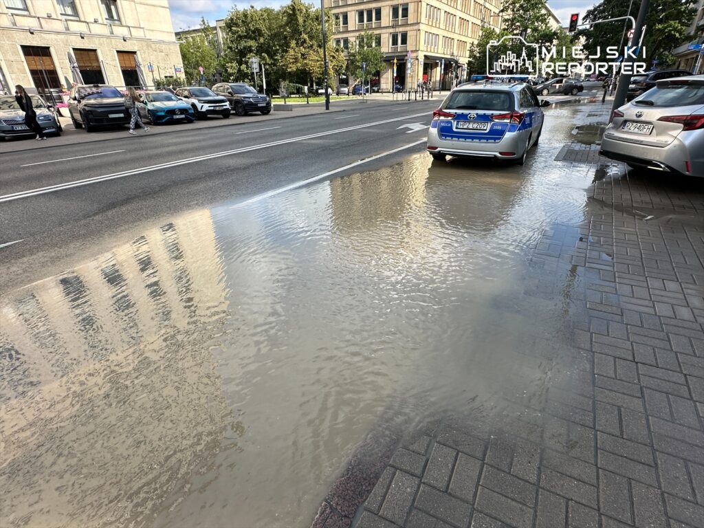 Na ulicy stoi kilka samochodów, a obok widać zalaną wodą nawierzchnię chodnika.