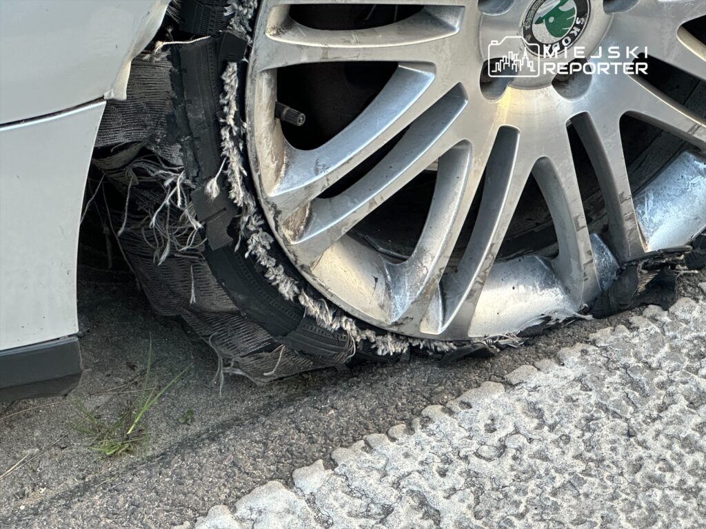 Zniszczona opona samochodowa z widocznymi uszkodzeniami na feldze, leżąca na chodniku.