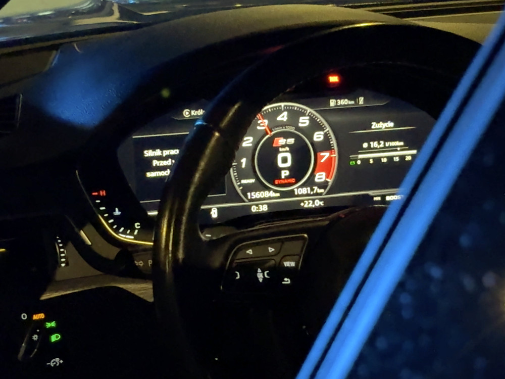 Wnętrze samochodu z widokiem na deski rozdzielczej, wskazujące prędkość 0 km/h i zużycie paliwa 16,2 l/100 km.