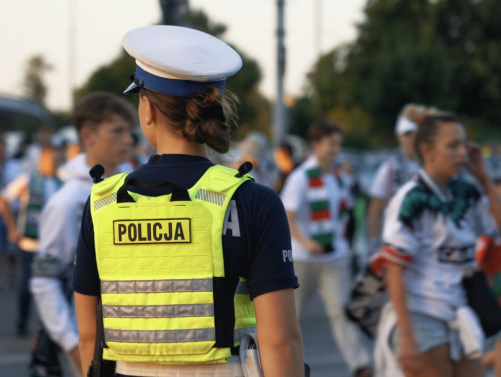Policjantka w kamizelce odblaskowej monitoruje tłum kibiców podczas wydarzenia na świeżym powietrzu.