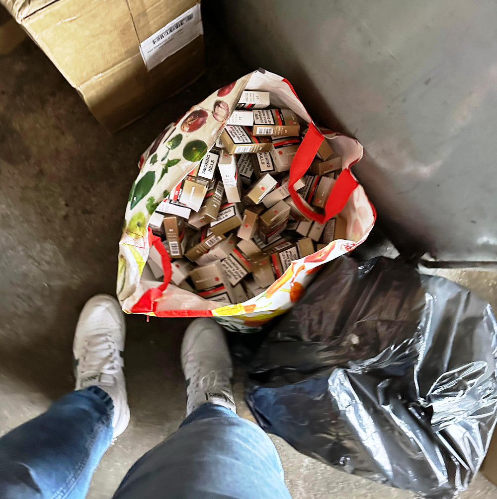 Torba z papierosami leży na podłodze obok czarnego worka na śmieci, w tle widoczny karton.