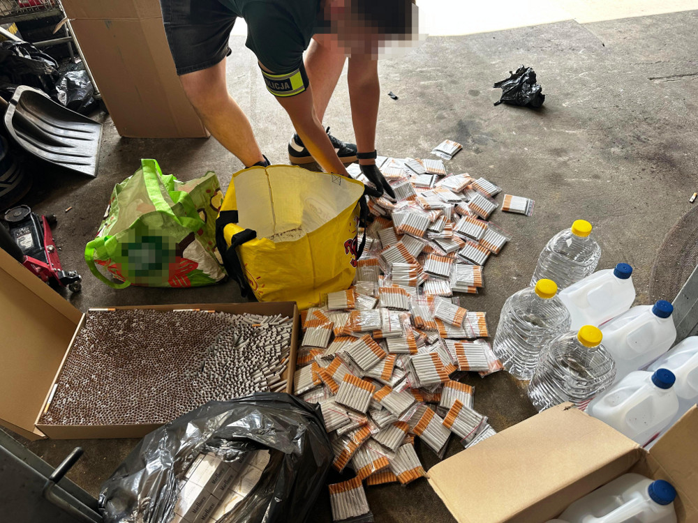 Mężczyzna w krótkich spodniach przeszukuje podłogę, wokół niego leżą paczki papierosów i plastikowe butelki z wodą.
