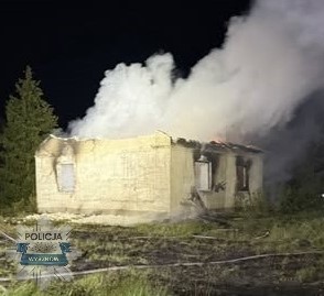 Pali się opuszczony budynek, z którego wydobywa się gęsty dym, w otoczeniu drzew.