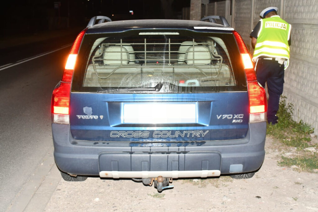 Policjant sprawdzający dokumenty przy zaparkowanym nieopodal samochodzie osobowym Volvo V70 XC w nocy.