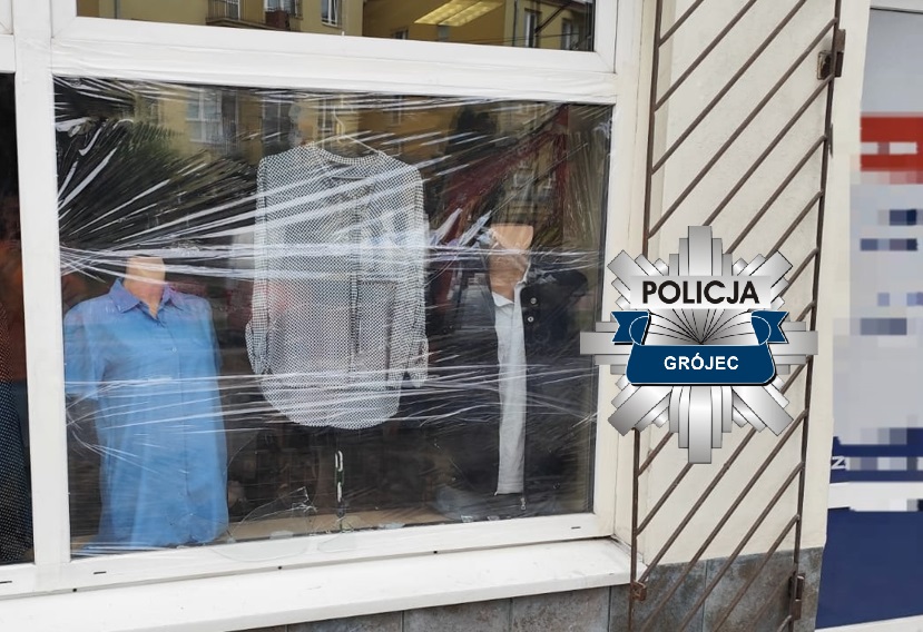 Manekiny w ubraniach zasłonięte folią stretch w witrynie sklepu, obok logo policji.