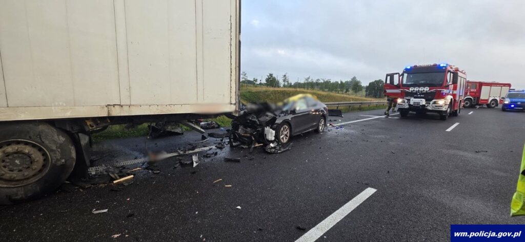 Wypadek drogowy z udziałem osobowego samochodu i ciężarówki na autostradzie, obok pojazdów ratunkowych.