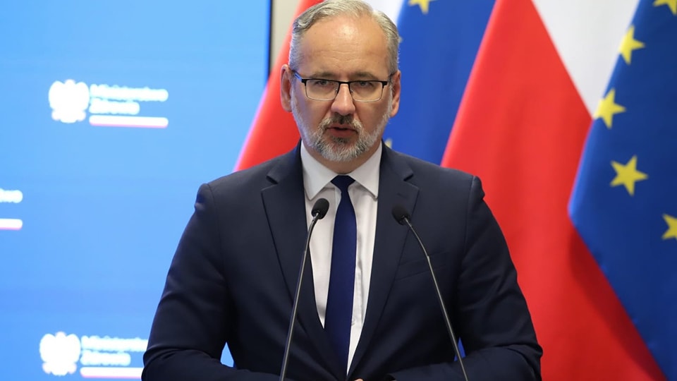 Mężczyzna w garniturze przemawia przy mikrofonie, w tle flagi Polski i Unii Europejskiej.