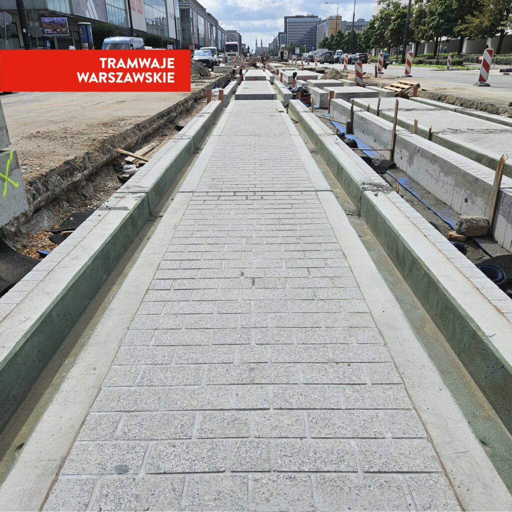 Nowa nawierzchnia tramwajowa z kostki brukowej w trakcie budowy, otoczona wykopami i betonowymi elementami.