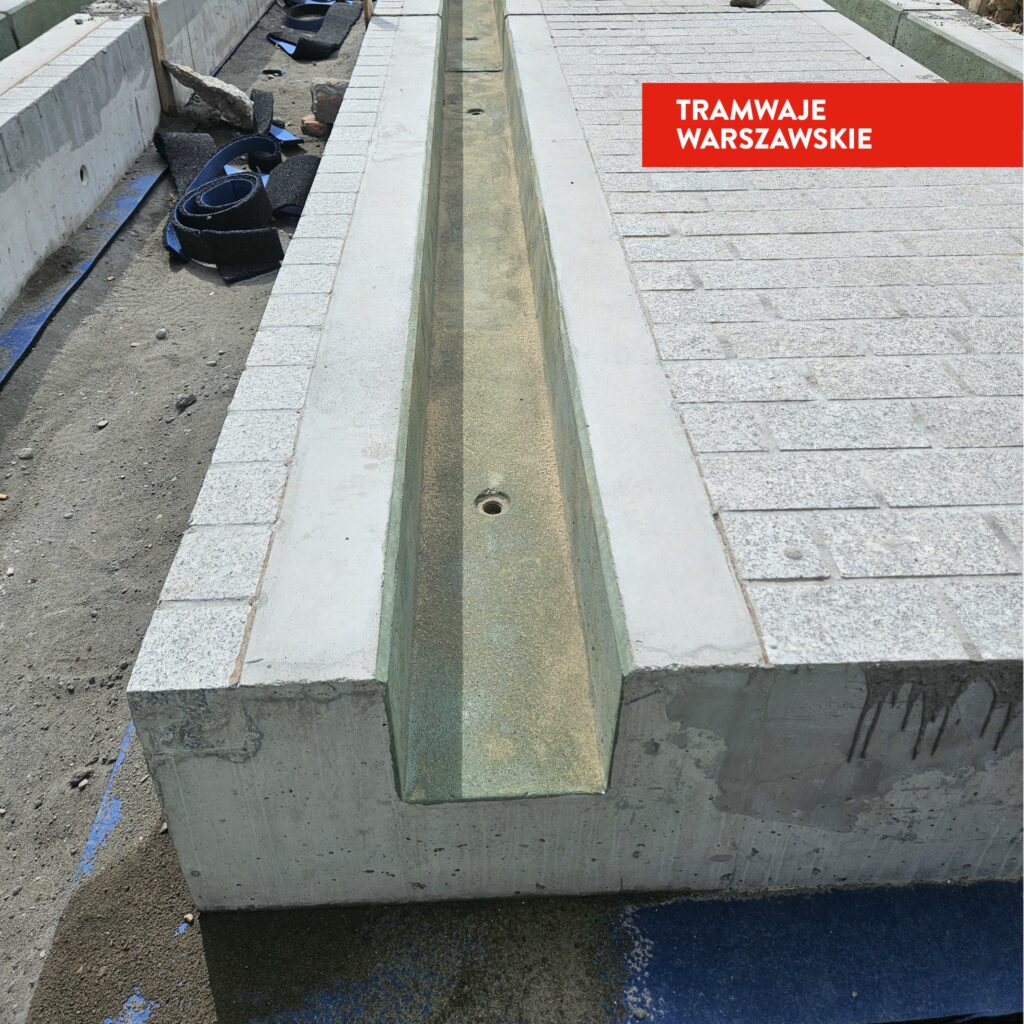 Betonowa konstrukcja torowiska tramwajowego z wyłożonymi kostkami brukowymi, w trakcie budowy.