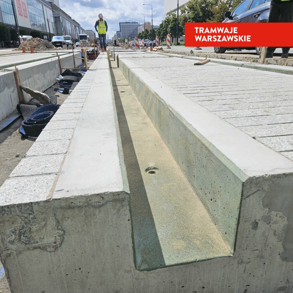Robotnicy w kamizelkach odblaskowych pracują nad nowym torowiskiem tramwajowym na placu budowy.