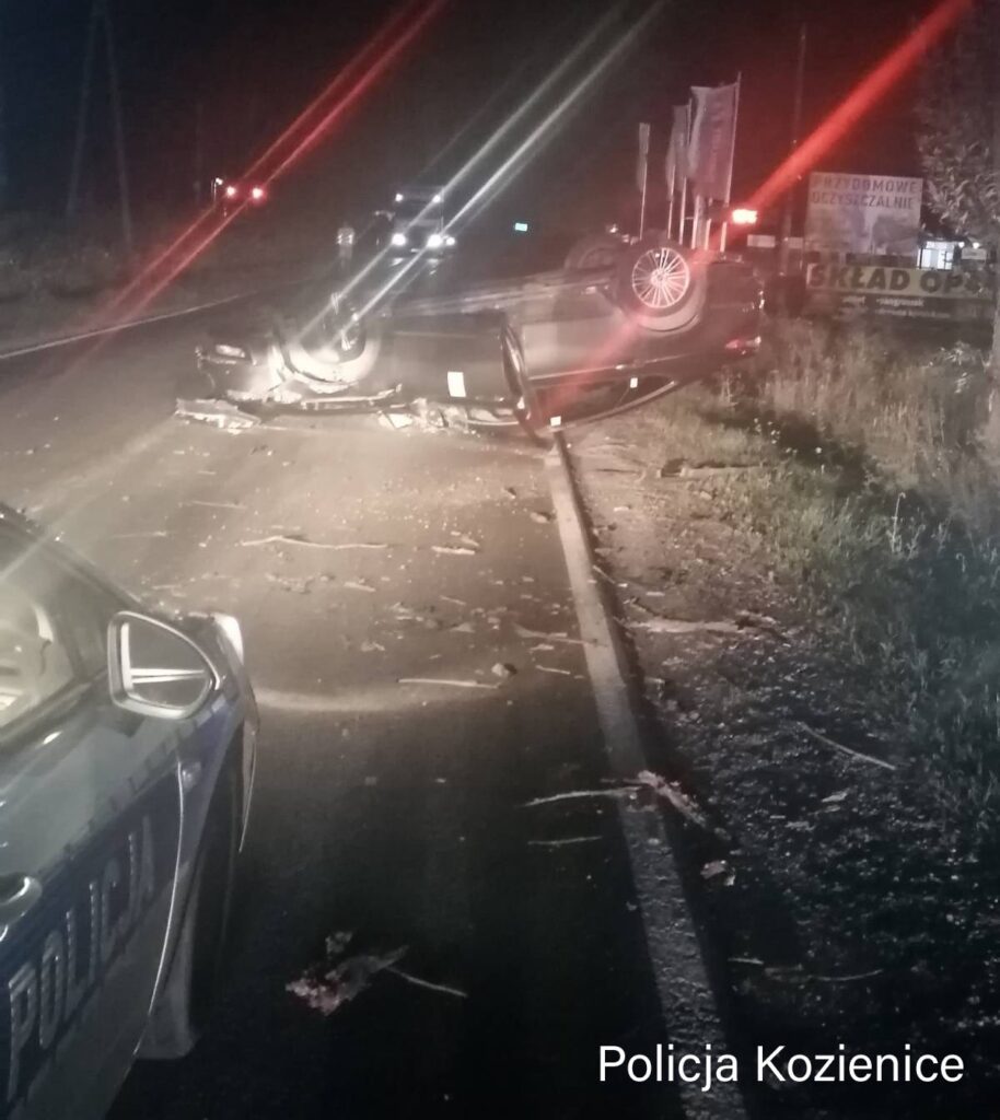Na drodze leży przewrócone auto, a obok znajdują się resztki po wypadku i radiowóz policji.