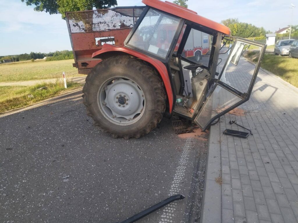 Traktor z otwartymi drzwiami stoi na poboczu drogi, obok leżą fragmenty szkła i odłamki.