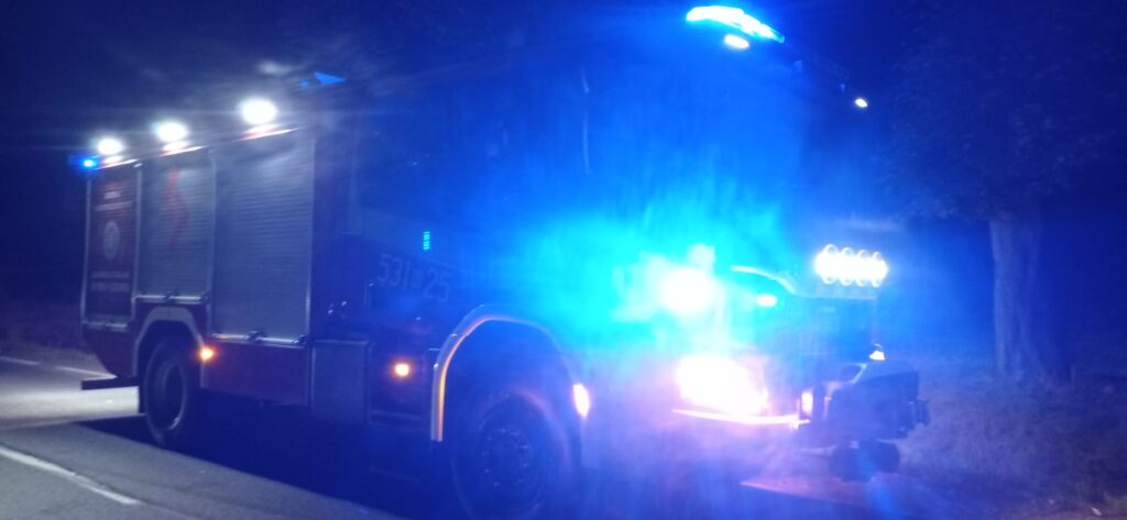 Wozidło strażackie z niebieskimi i czerwonymi światłami zatrzymane na drodze nocą.