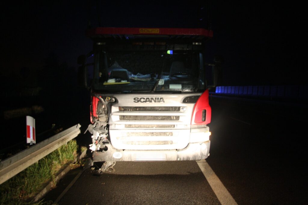 Czerwony i srebrny ciężarówka marki Scania z uszkodzoną przednią częścią stoi na drodze nocą.