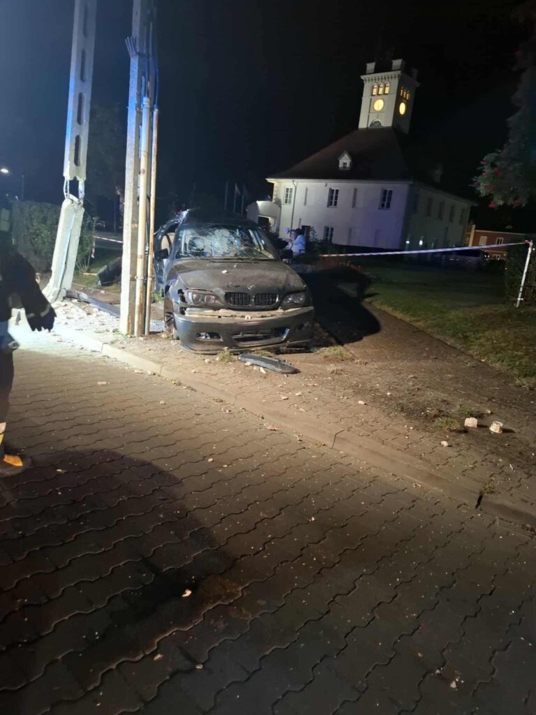 Samochód osobowy uderzył w słup elektryczny obok budynku z wieżą zegarową w nocy, otoczony przez funkcjonariuszy.