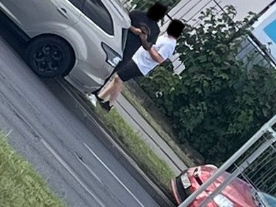 Dwaj mężczyźni rozmawiają obok zaparkowanego samochodu w miejskim otoczeniu.