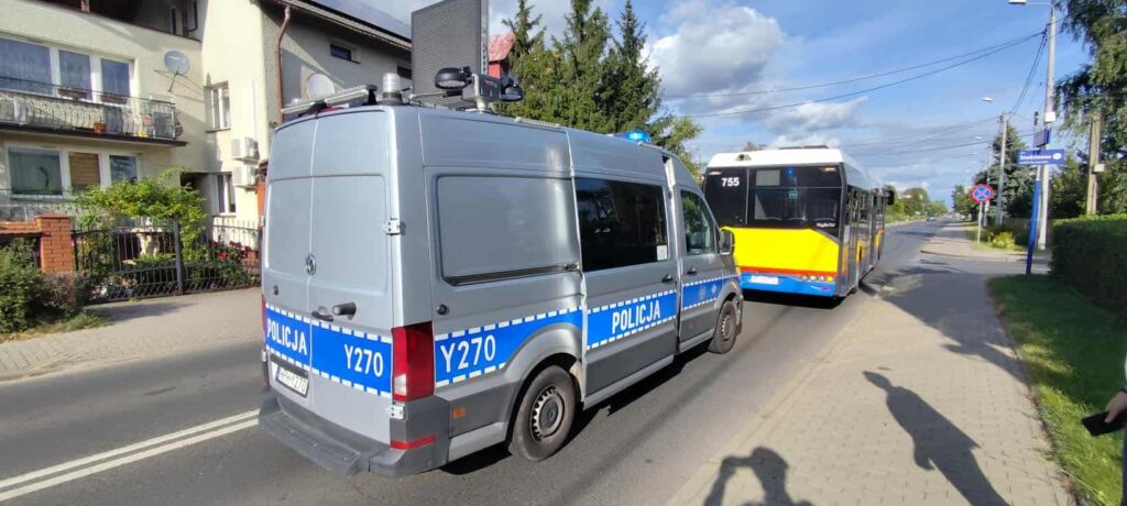 Radiowóz policyjny zatrzymany na poboczu drogi obok autobusu miejskiego w słoneczny dzień.