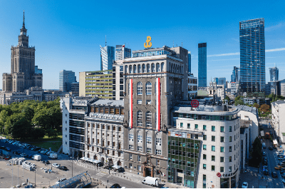 Nowoczesne wieżowce otaczające historyczny budynek z czerwonymi i białymi detalami w centrum miasta.